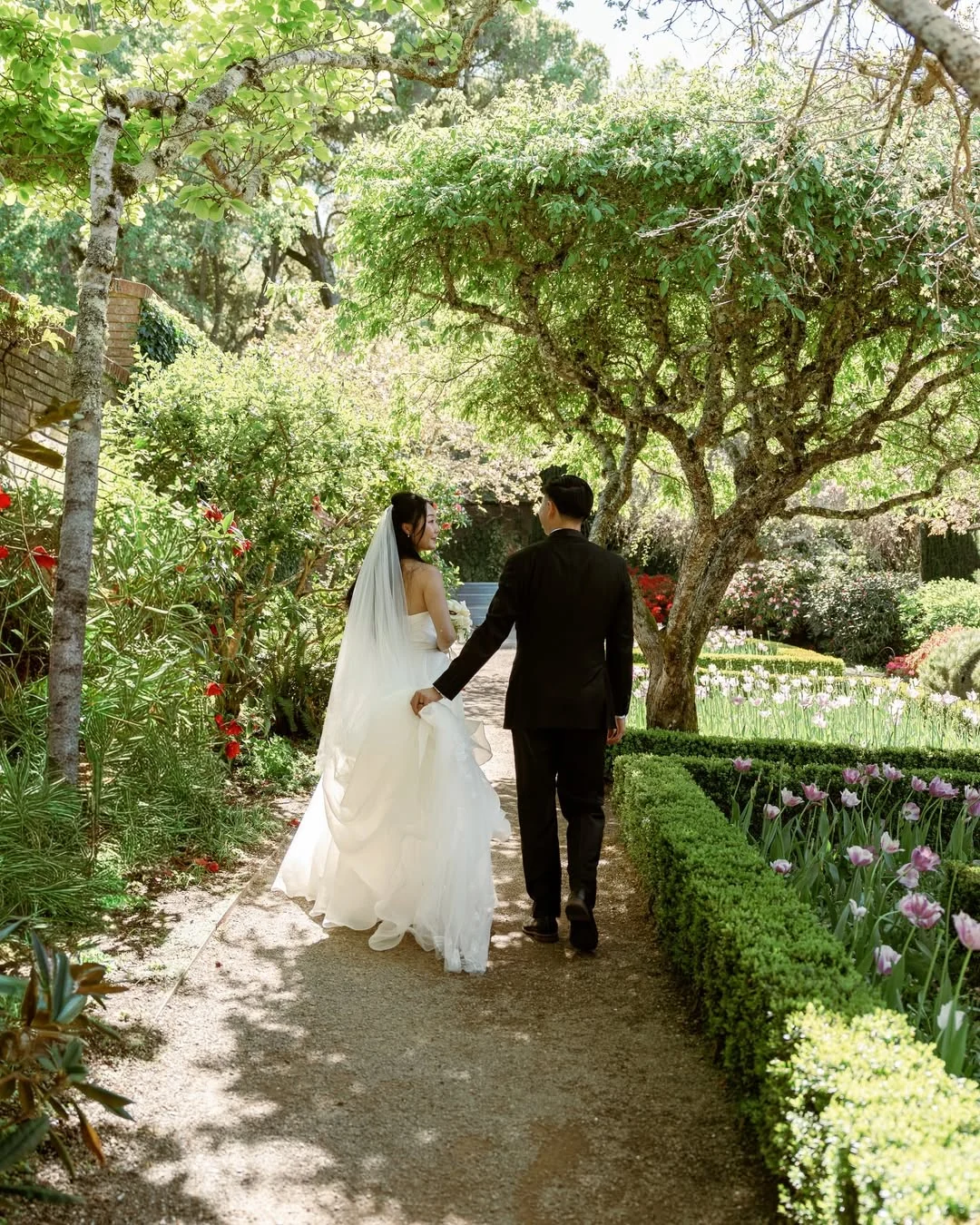Newlyweds walking hand in hand beneath a leafy garden arch